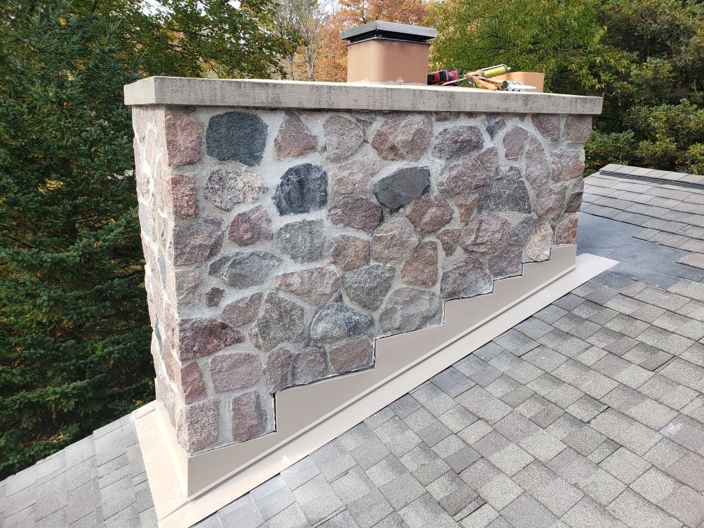 A stone chimney on top of a roof with trees in the background.