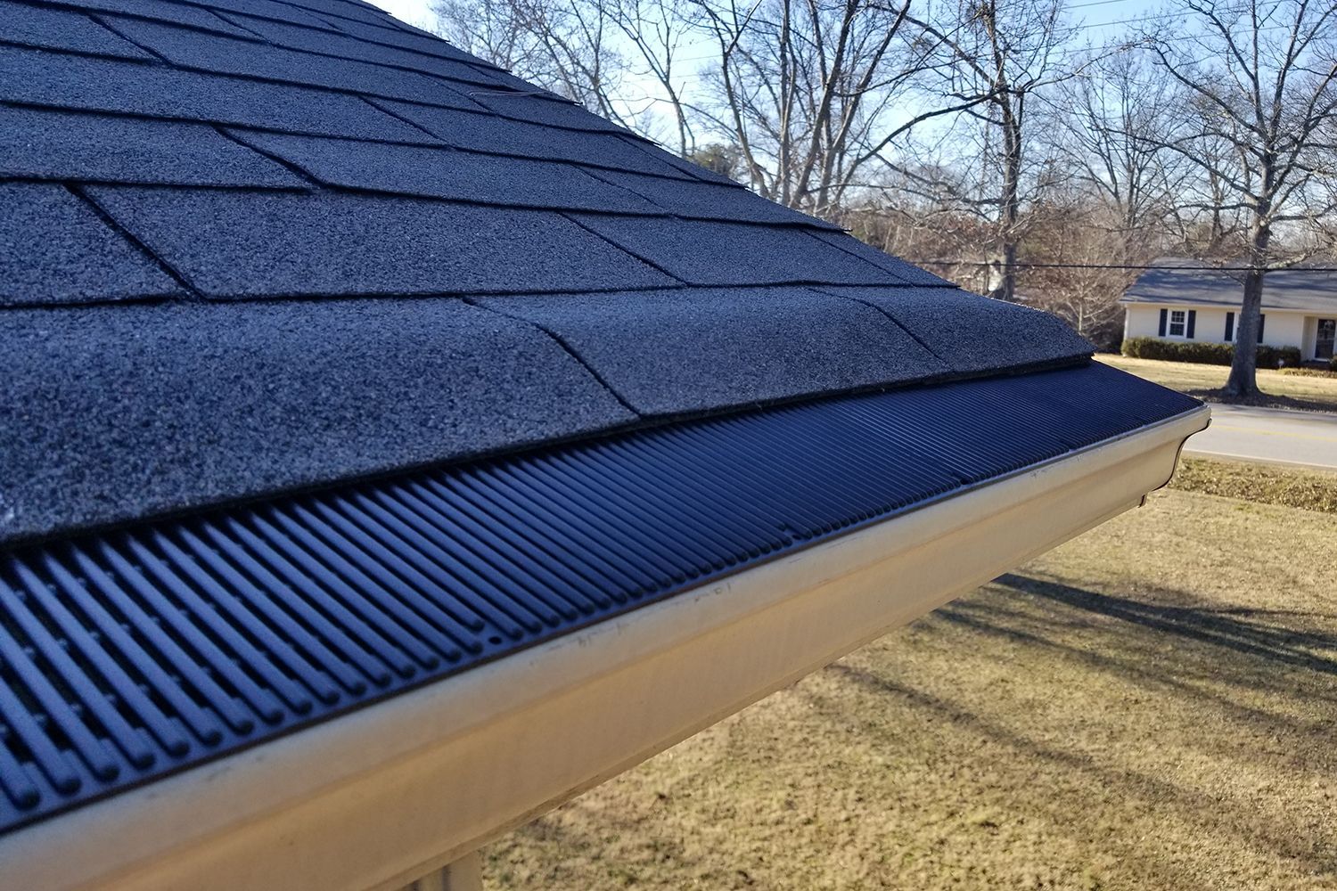 A close up of a gutter on a roof with a house in the background.