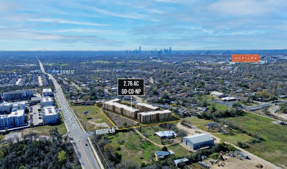 Aerial view of a suburban area with roads, buildings, and a distant city skyline under clear blue sky