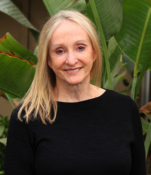 A woman in a black shirt is smiling in front of a plant.