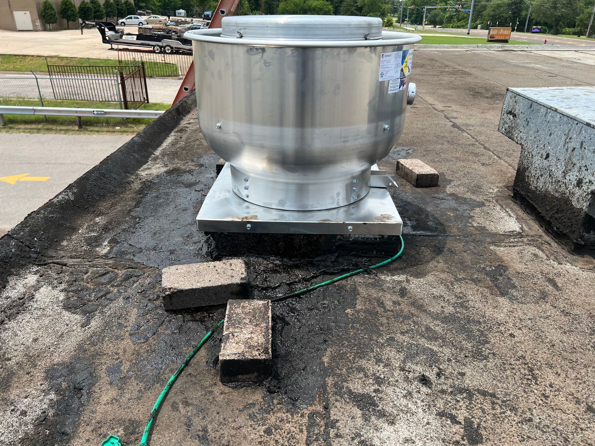 A large metal fan is sitting on top of a roof next to a green hose.