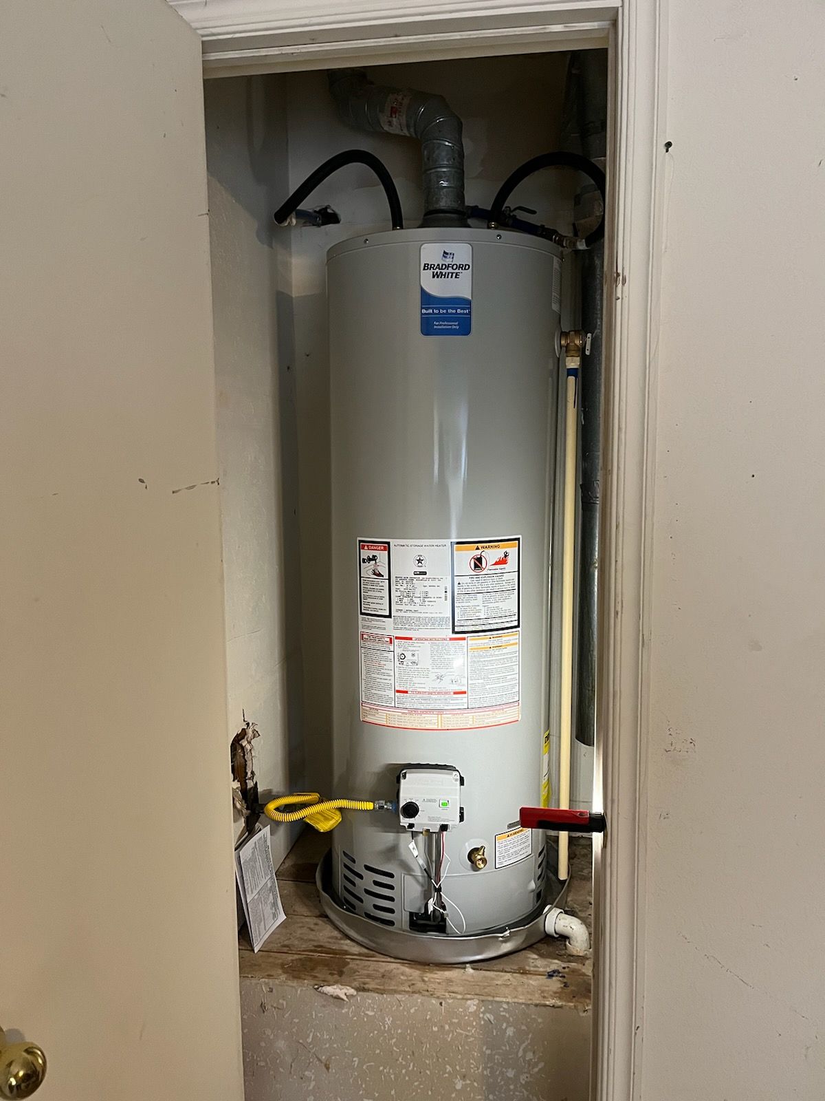A water heater is sitting in a closet next to a door.