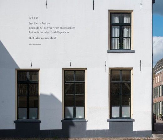 Een wit gebouw met een gedicht over het Hier en Nu, wat aansluit bij mijn manier van werken vanuit de Gestalttherapie