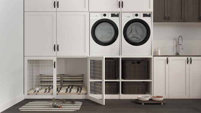 A laundry room with two washers and dryers and a dog cage.