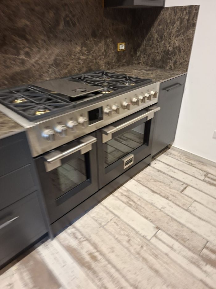 Cucina moderna con piano cottura a gas in acciaio inox, paraschizzi in marmo scuro e pavimento in legno chiaro.