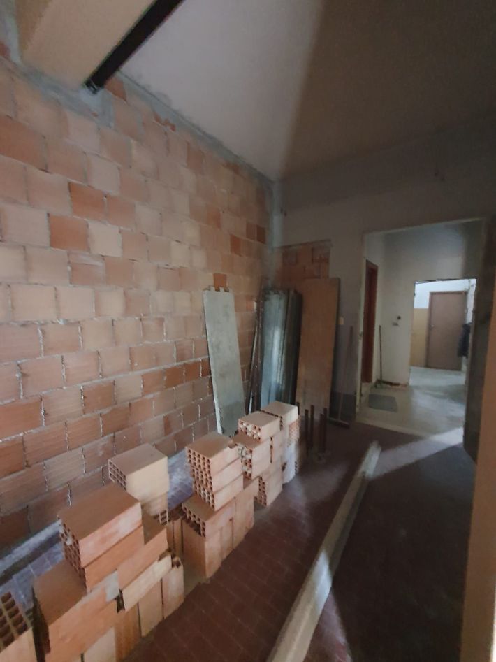 Interno non rifinito con pareti in mattoni a vista, mattoni accatastati e una porta che conduce a un'altra stanza.