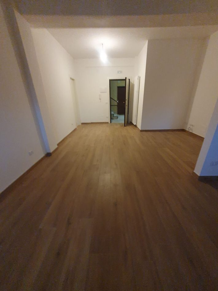 Stanza vuota con pavimento in legno, pareti bianche e una porta in fondo.