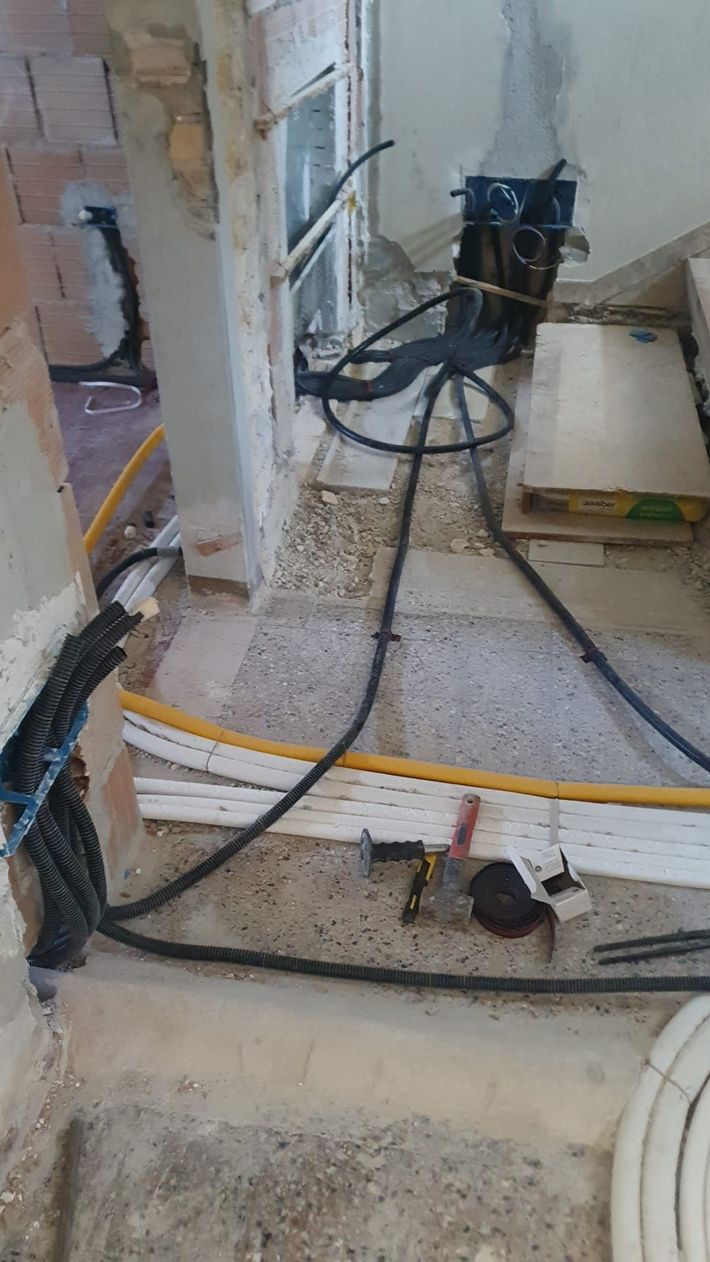 Interni in fase di ristrutturazione con cavi elettrici a vista, attrezzi e detriti su un pavimento di cemento.