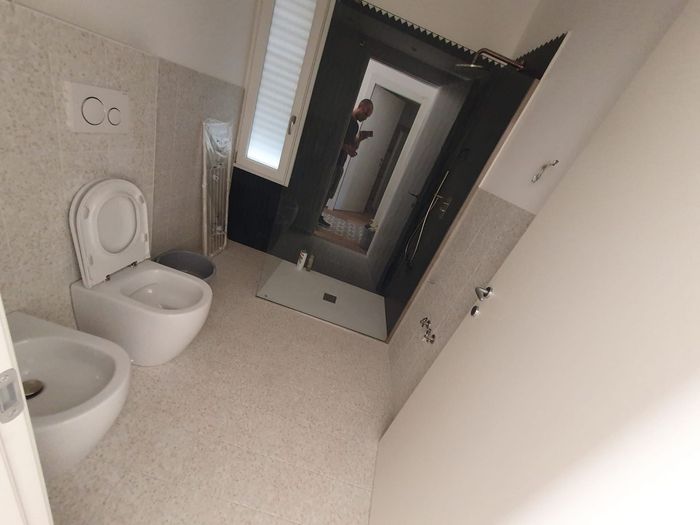 Bagno moderno con WC bianco, lavabo e vasca da bagno sotto un lucernario, visibile dalla porta.