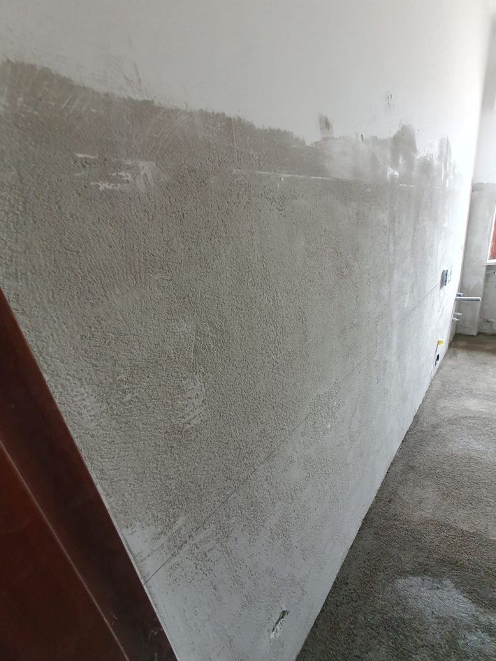 Parete bianca appena intonacata con una sezione grigia grezza in un corridoio o in una tromba delle scale.