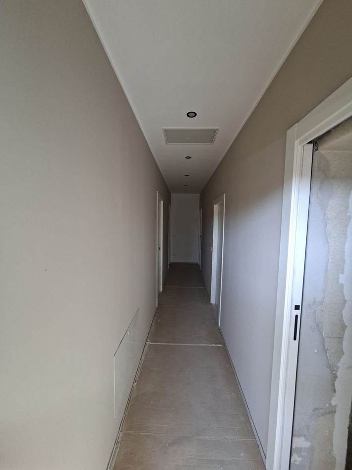 Stretto corridoio bianco con porte su entrambi i lati e pavimento piastrellato, visto in direzione di una porta scura in fondo.