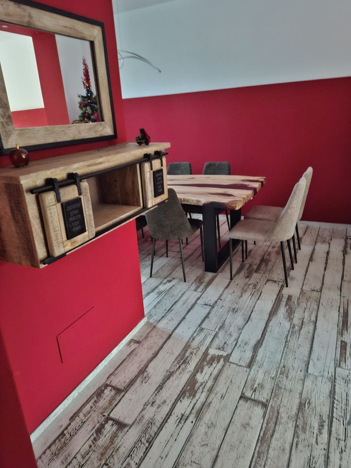 Sala da pranzo con pareti rosse, tavolo in legno, sedie scure e una mensola a muro sotto uno specchio.