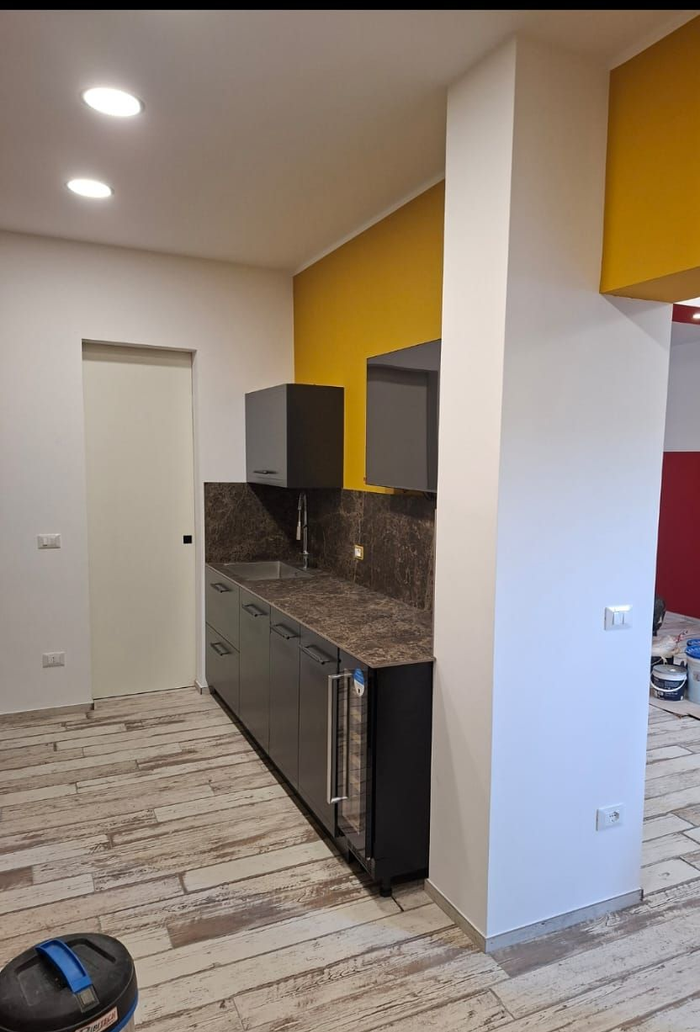 Piccola cucina con pareti a contrasto gialle, mobili grigi, piano di lavoro in granito e porta bianca sullo sfondo.