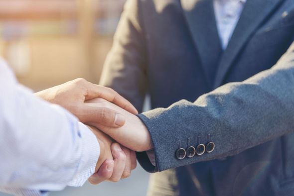 Two people shaking hands, with one person placing their other hand on top in a gesture of support or agreement.