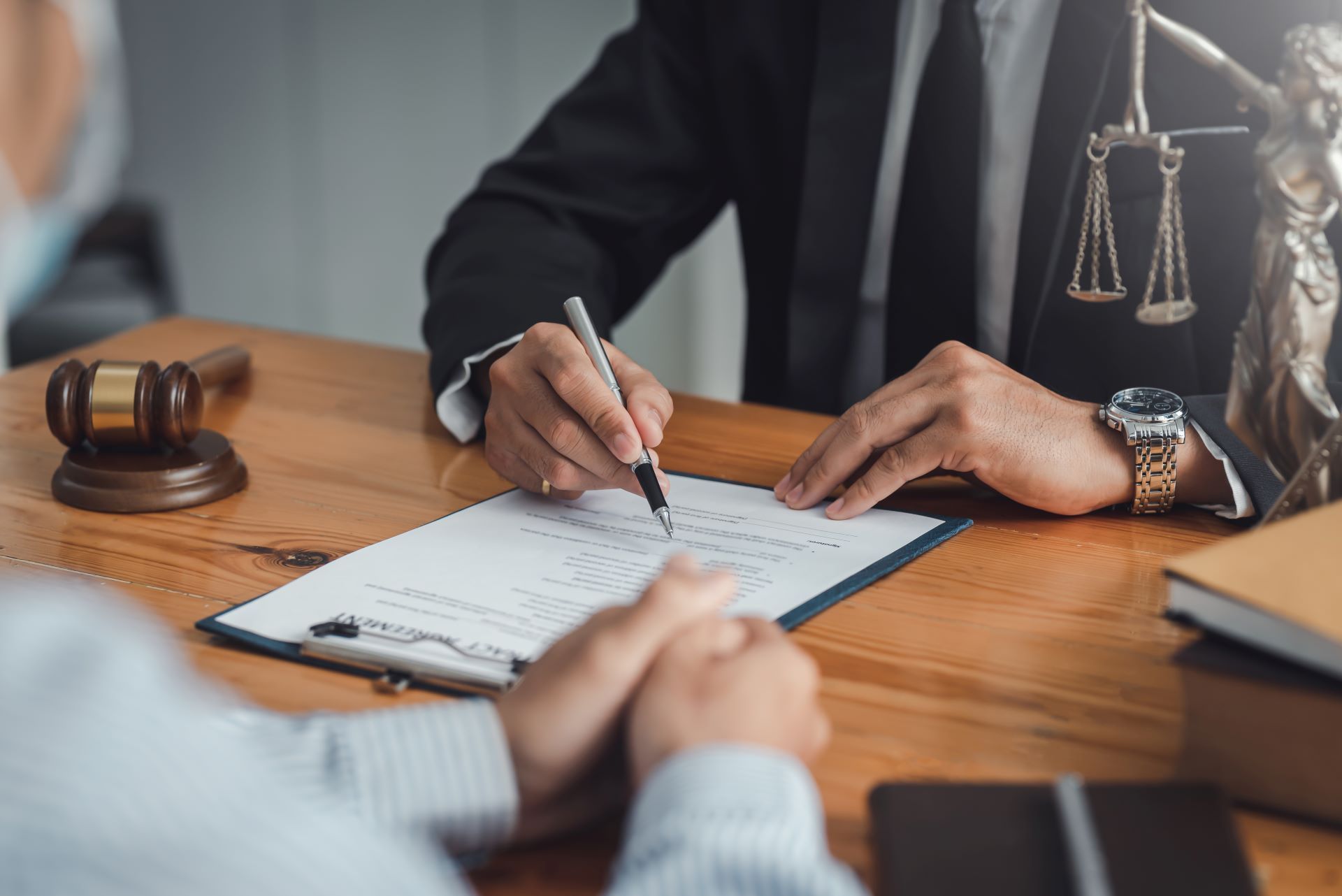 A professional in a suit and tie points to a legal document on a wooden desk next to a judge's gavel and scales of justice.