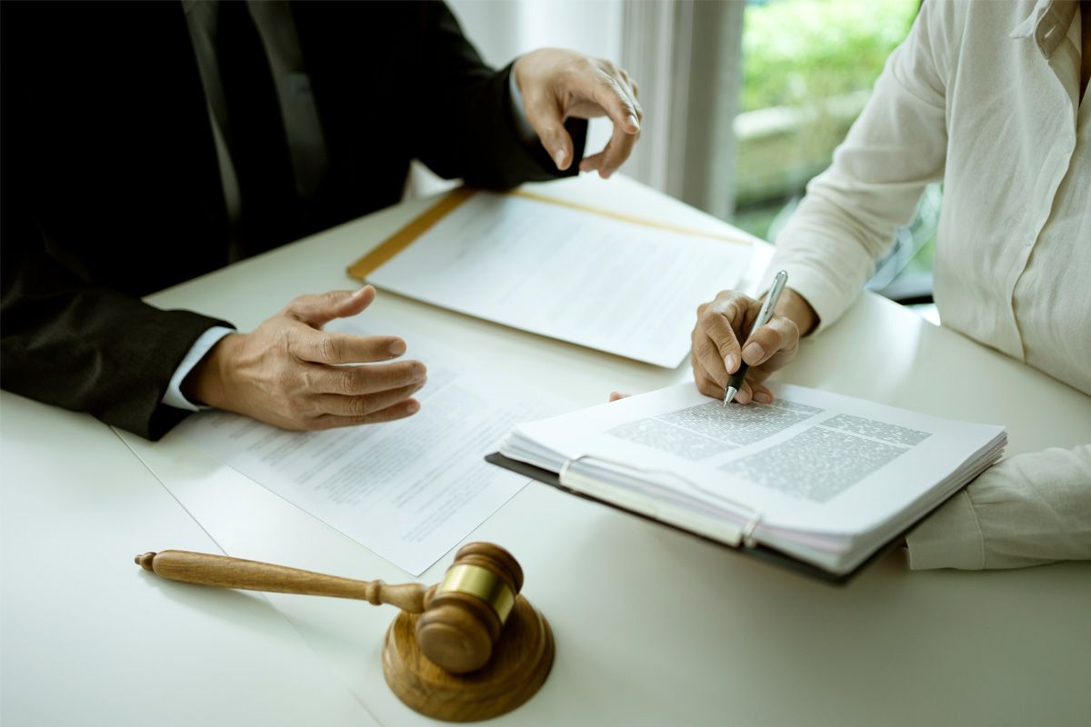 A person in a suit and a person in a white shirt reviewing documents at a table with a wooden gavel.