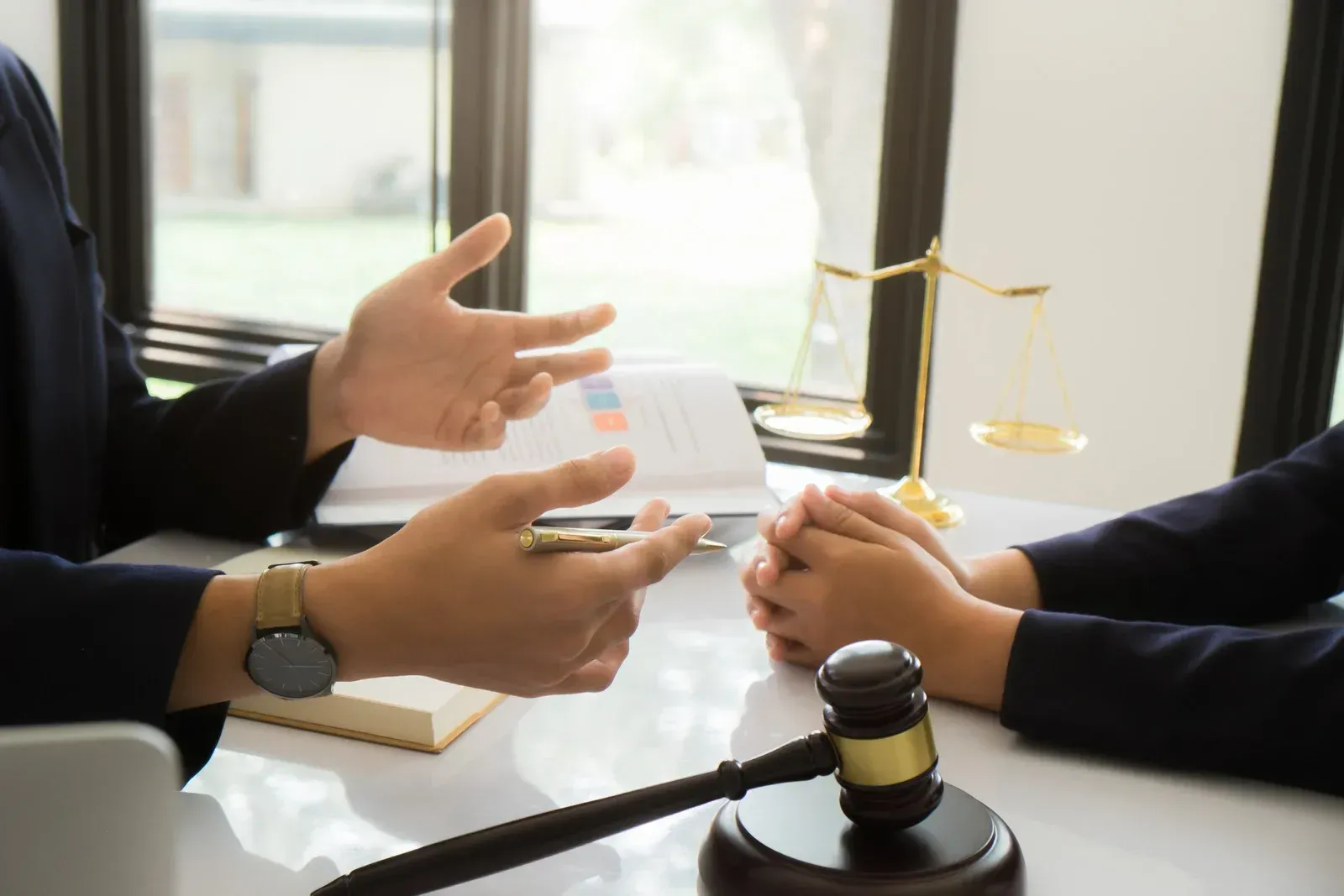 Two people sitting at a table with a judge’s gavel and scales of justice, discussing legal matters.