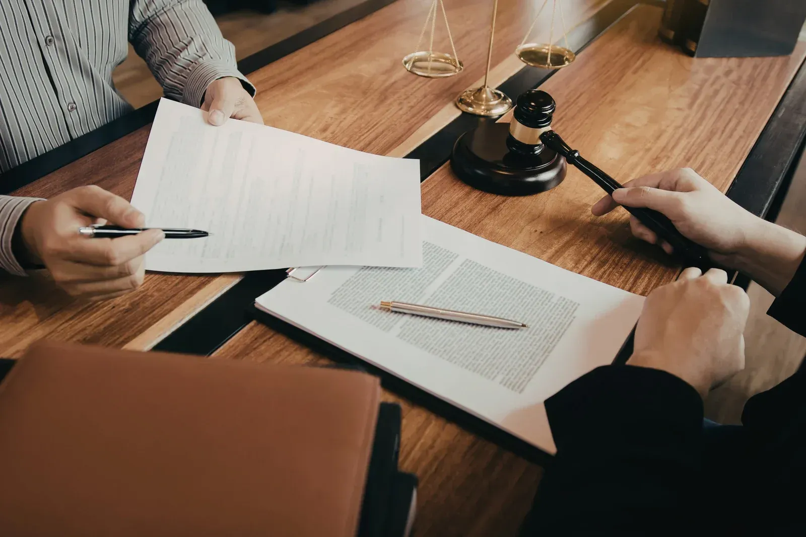 Two people reviewing legal documents on a wooden desk with a gavel and balance scale nearby.