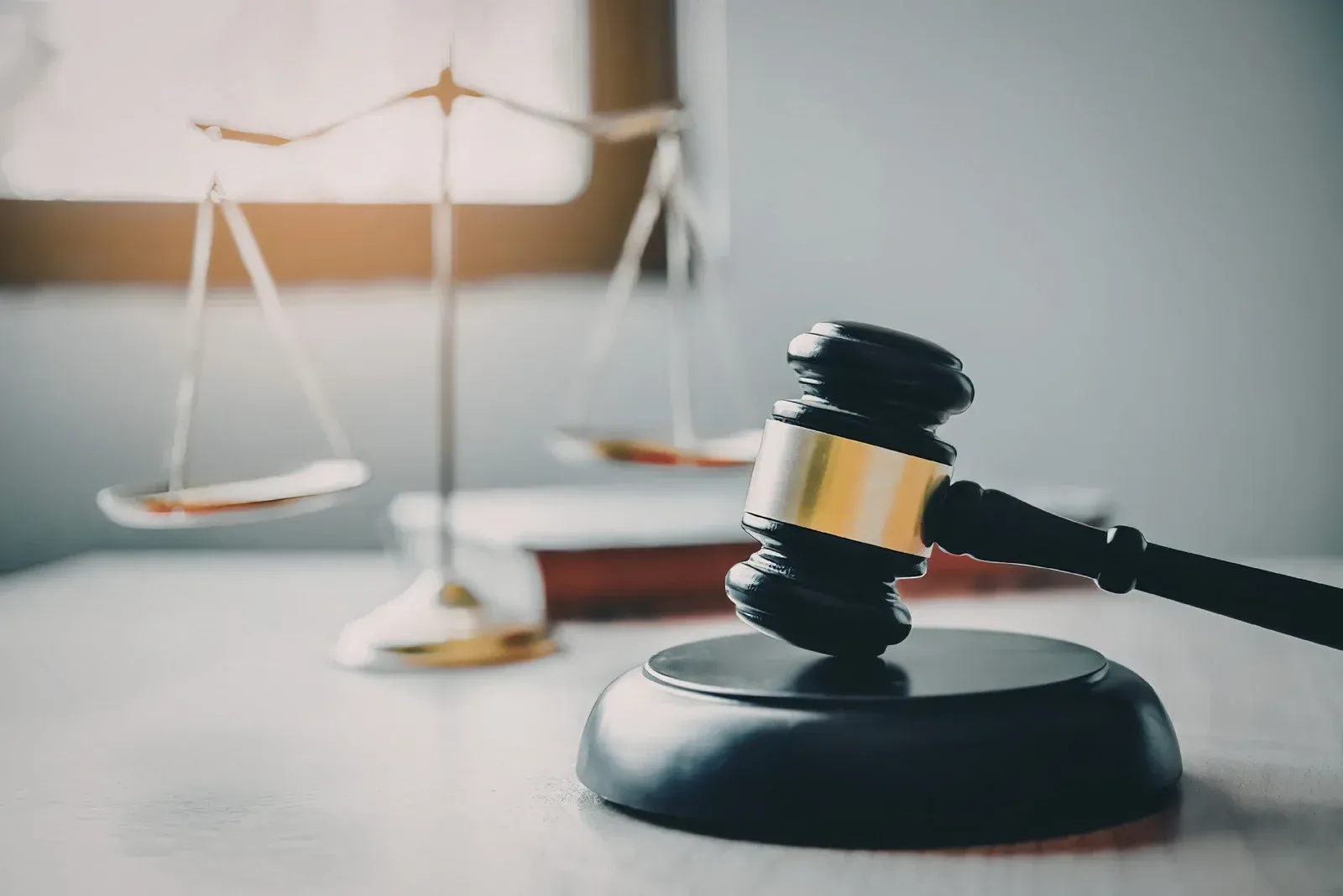A wooden judge's gavel rests on a sounding block in the foreground, with a golden scale of justice in the blurred background.