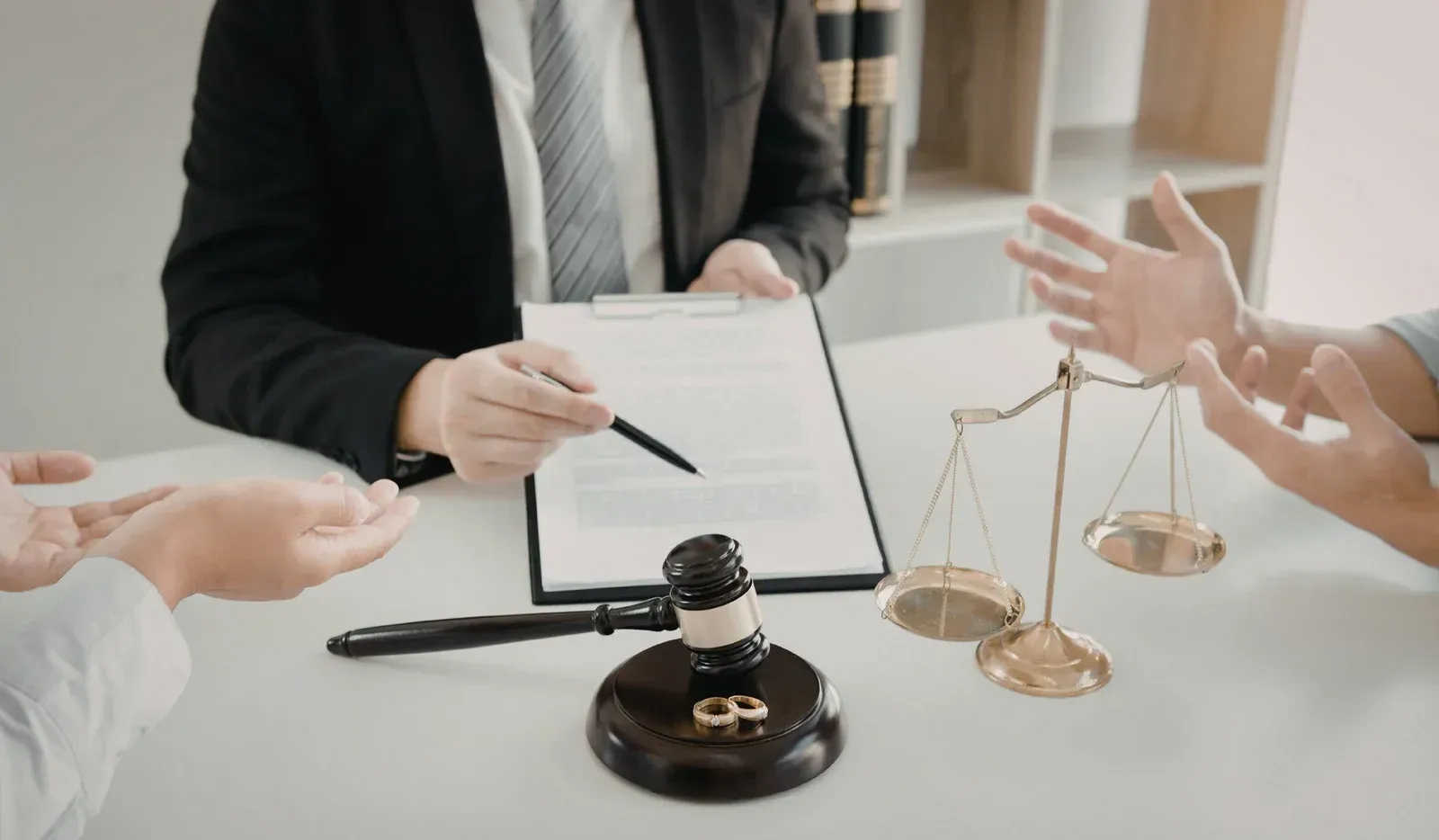 A lawyer reviews a document with clients at a desk featuring a wooden gavel and golden scales of justice.
