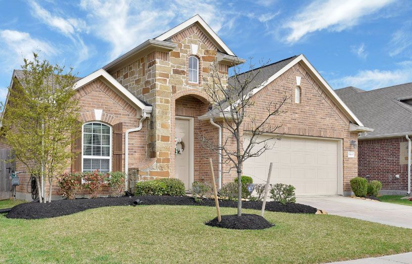 House with brick and stone facade, arched entryway, and manicured lawn under a blue sky.