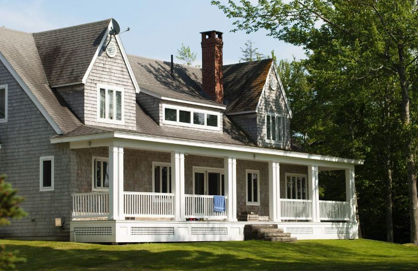 Gray shingled house with a white porch, chimney, and green lawn.