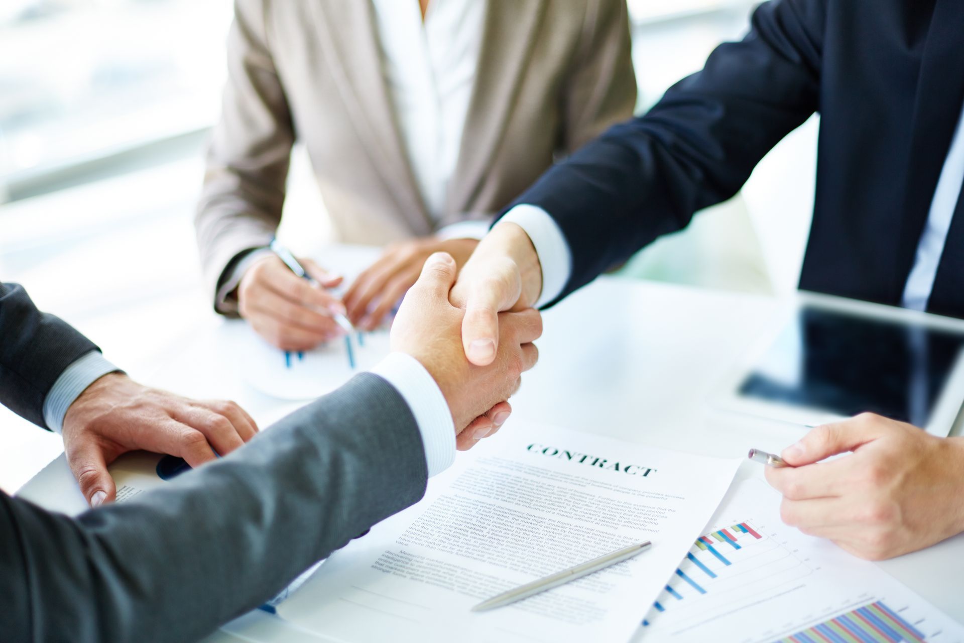 A group of business people are shaking hands over a table.