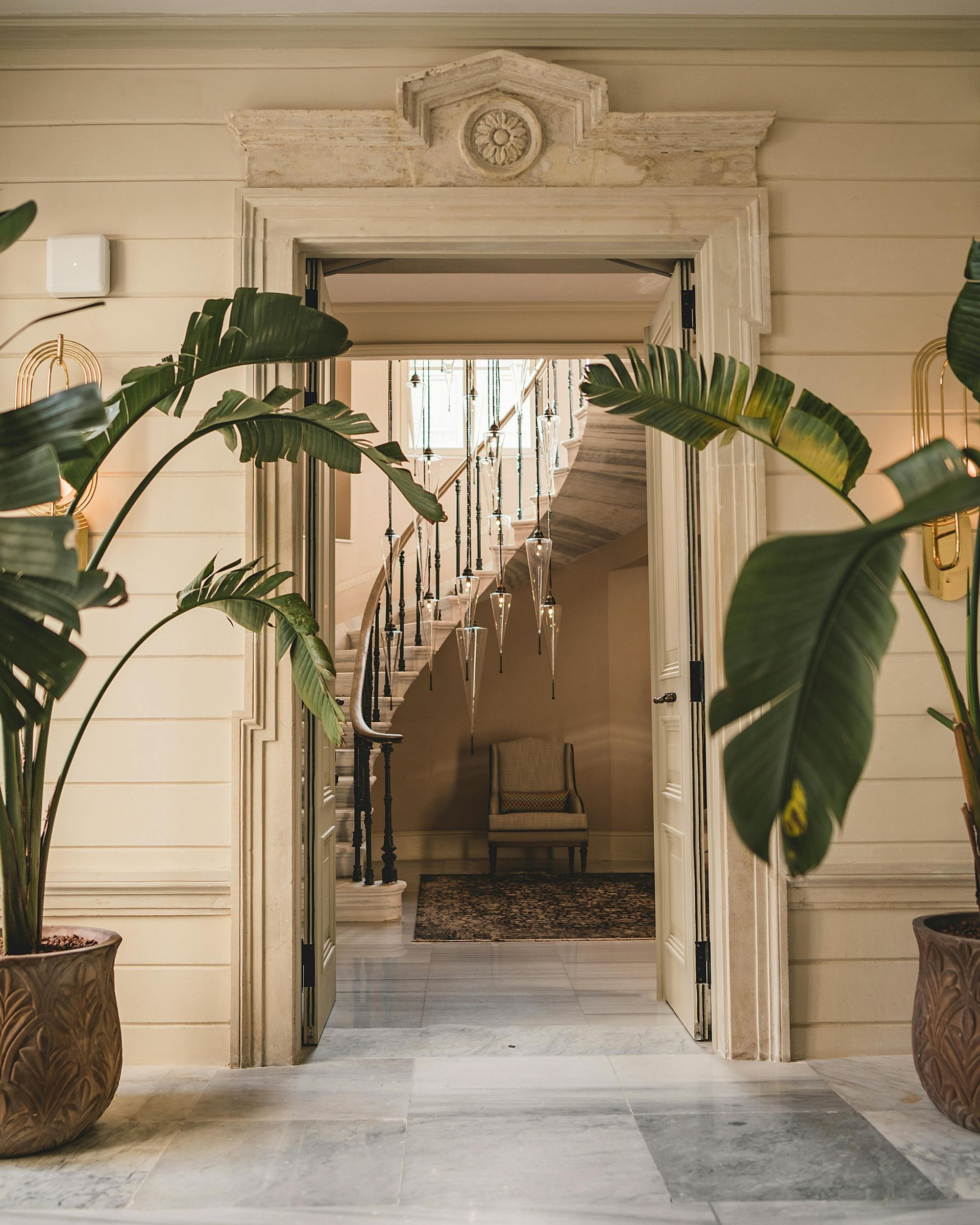 Ornate doorway frames a winding staircase; indoor plants flank the entrance.