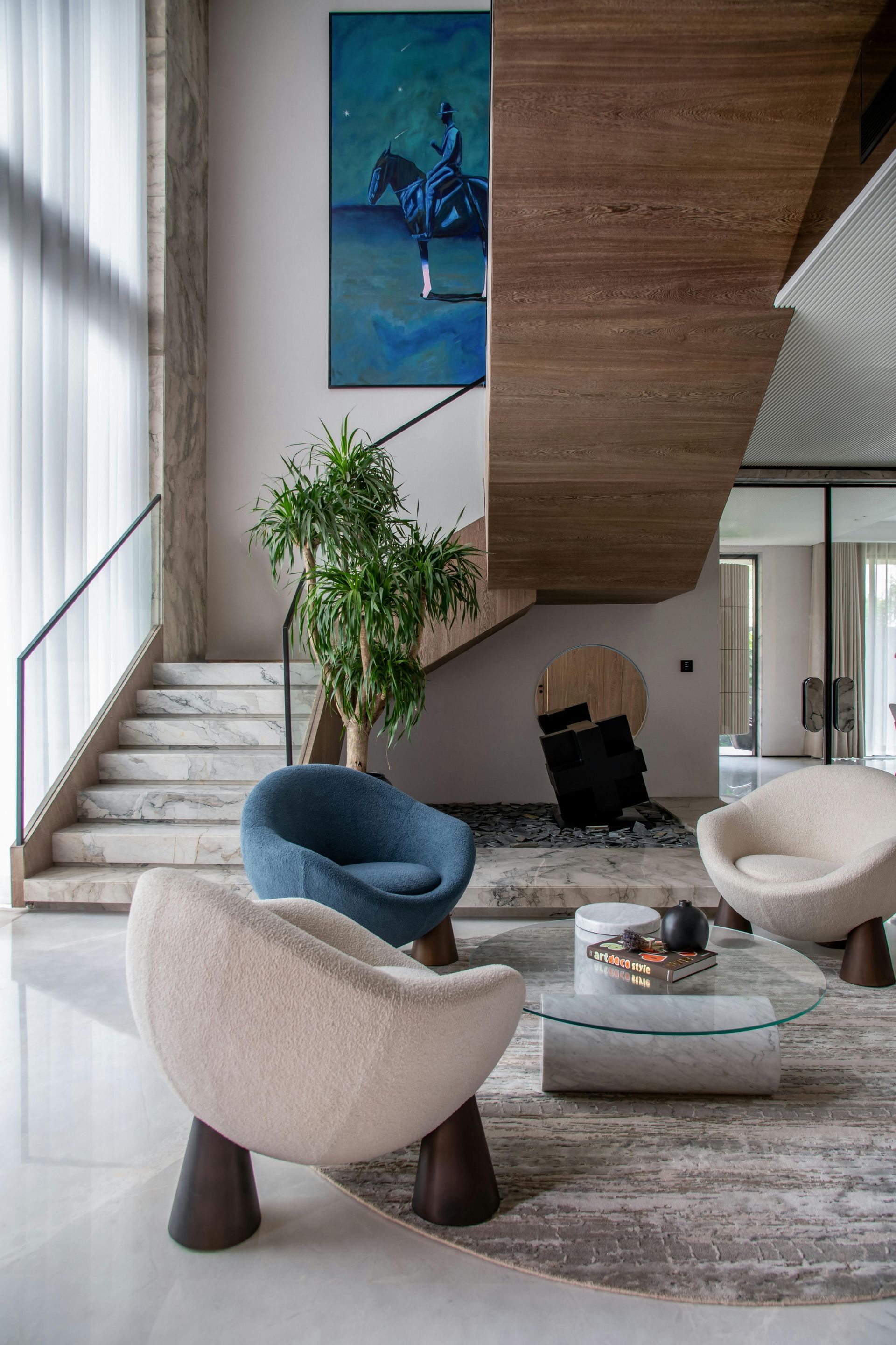 Modern living room with stairs, unique chairs, artwork, and a plant.