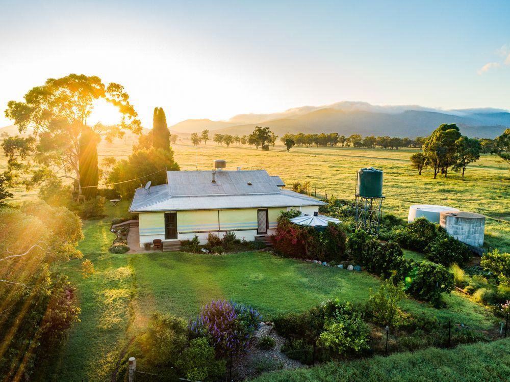 Sunlit Farmhouse With Green Lawn, Water Tank, and Mountains — Kellie O'Malley Conveyancing In Lake Munmorah, NSW
