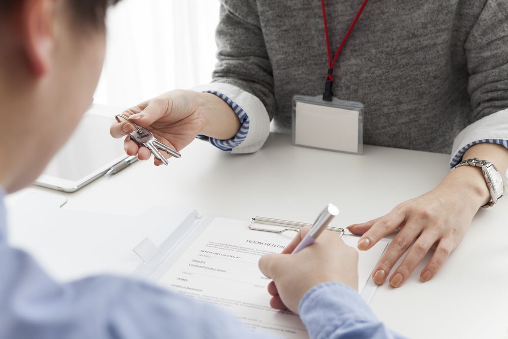 Person Signing a Document, Receiving Keys From Another Person at a Desk — Kellie O'Malley Conveyancing In Lake Munmorah, NSW
