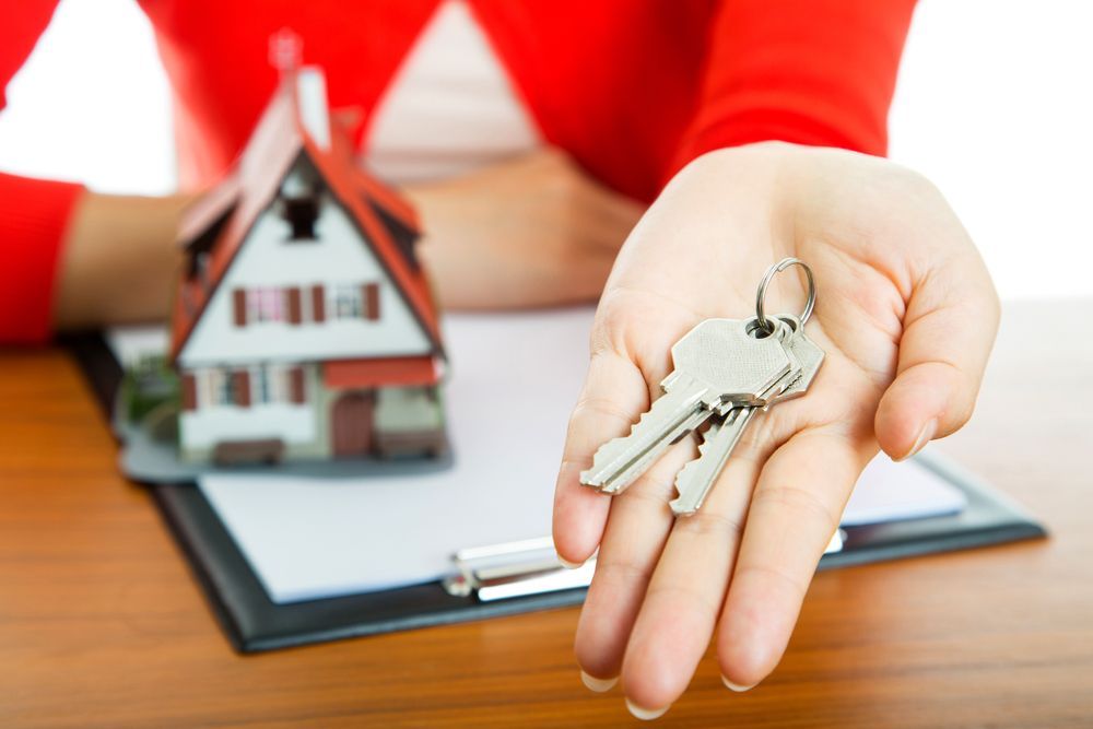 Hand Holding Keys, Miniature House, and Documents on a Desk — Kellie O'Malley Conveyancing In Cessnock, NSW