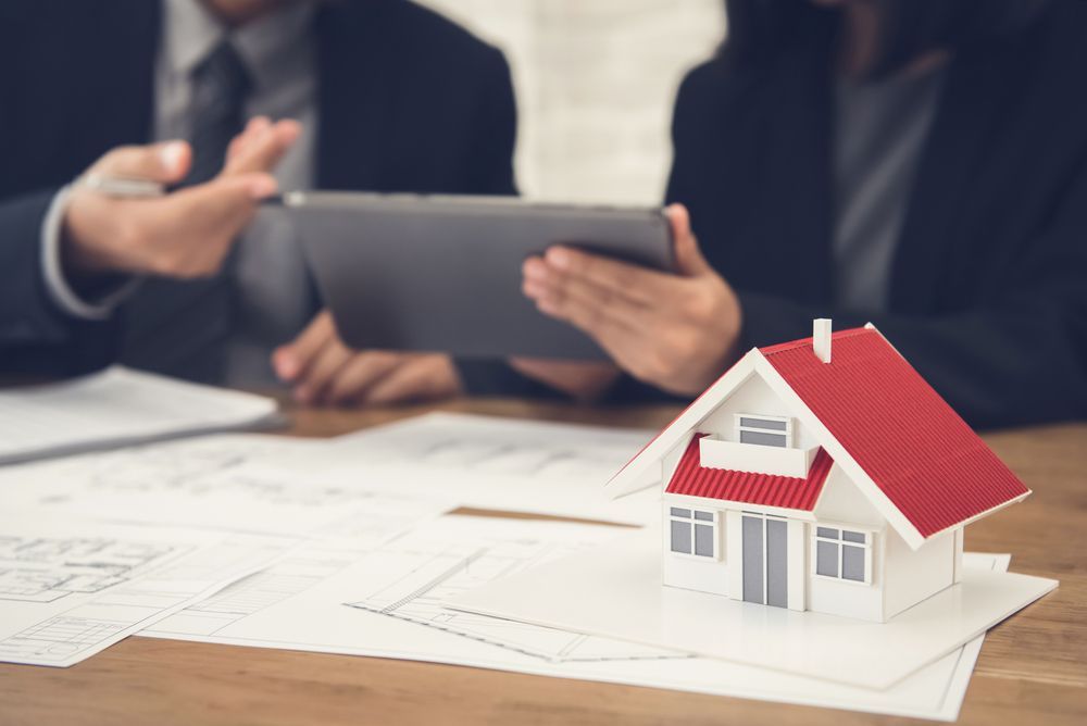 Two People Reviewing a Tablet With a Miniature House on a Desk — Kellie O'Malley Conveyancing In Mid North Coast, NSW