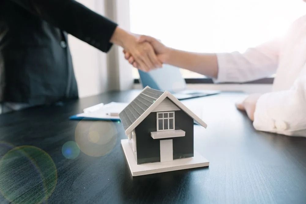 Miniature House on Table With People Shaking Hands — Kellie O'Malley Conveyancing In Lake Munmorah, NSW