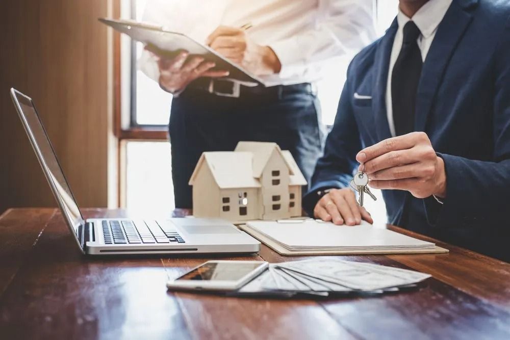Two People in Suits at a Desk With a House Model, Laptop, and Money — Kellie O'Malley Conveyancing In Newcastle, NSW