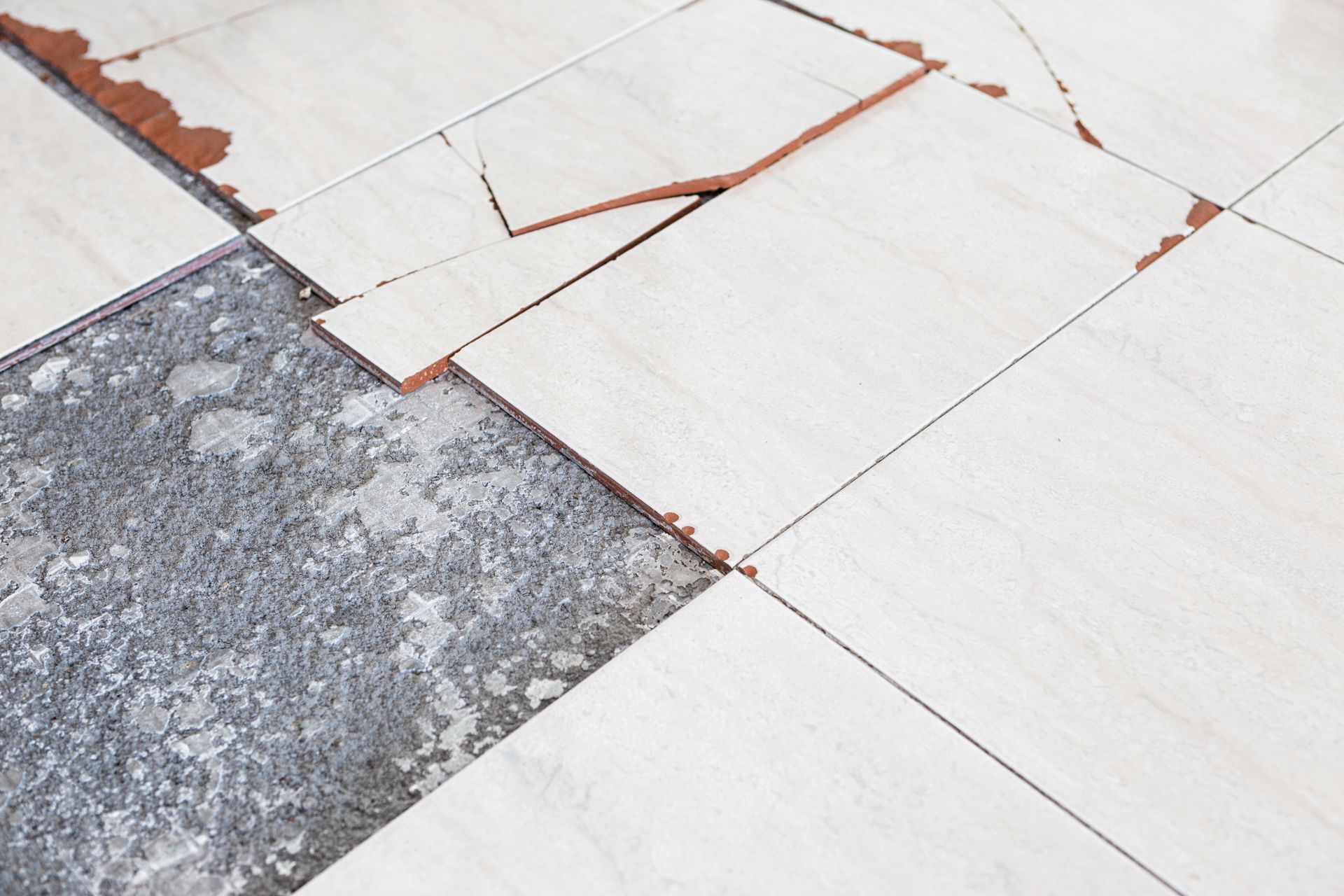 Broken and cracked ceramic floor tiles with an empty space revealing the rough concrete subfloor below.