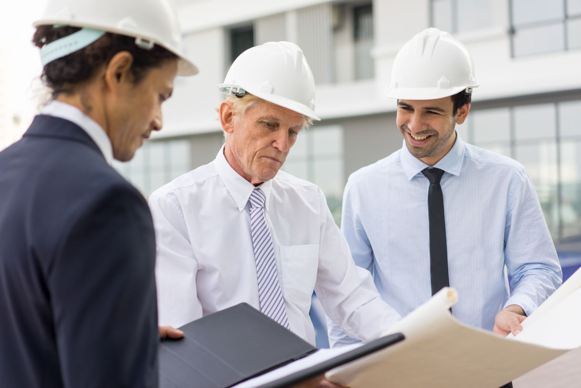 Three people in hard hats looking at building plans outdoors.