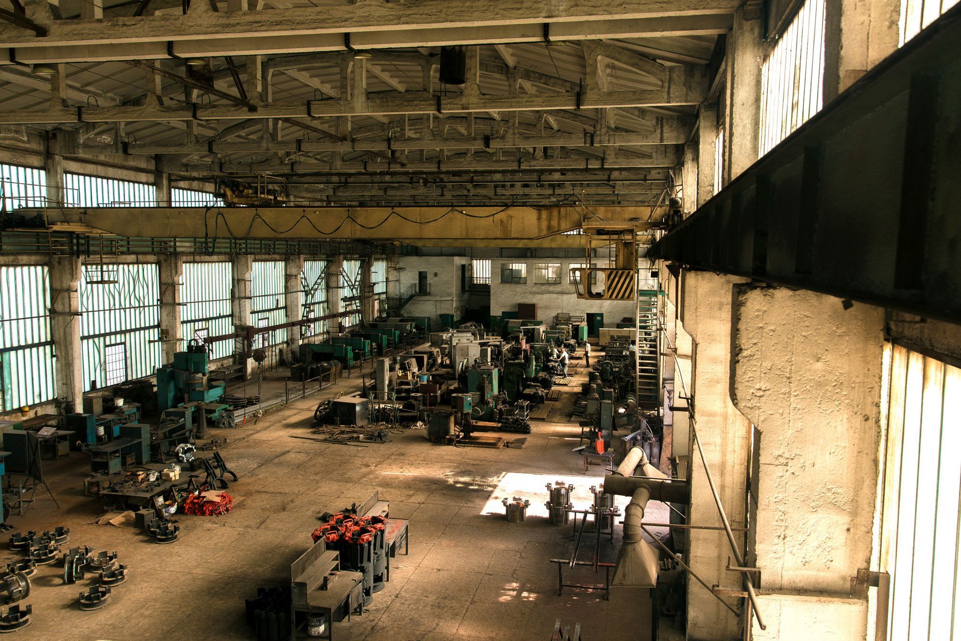 Industrial warehouse interior with machinery, dusty concrete floor, large windows.