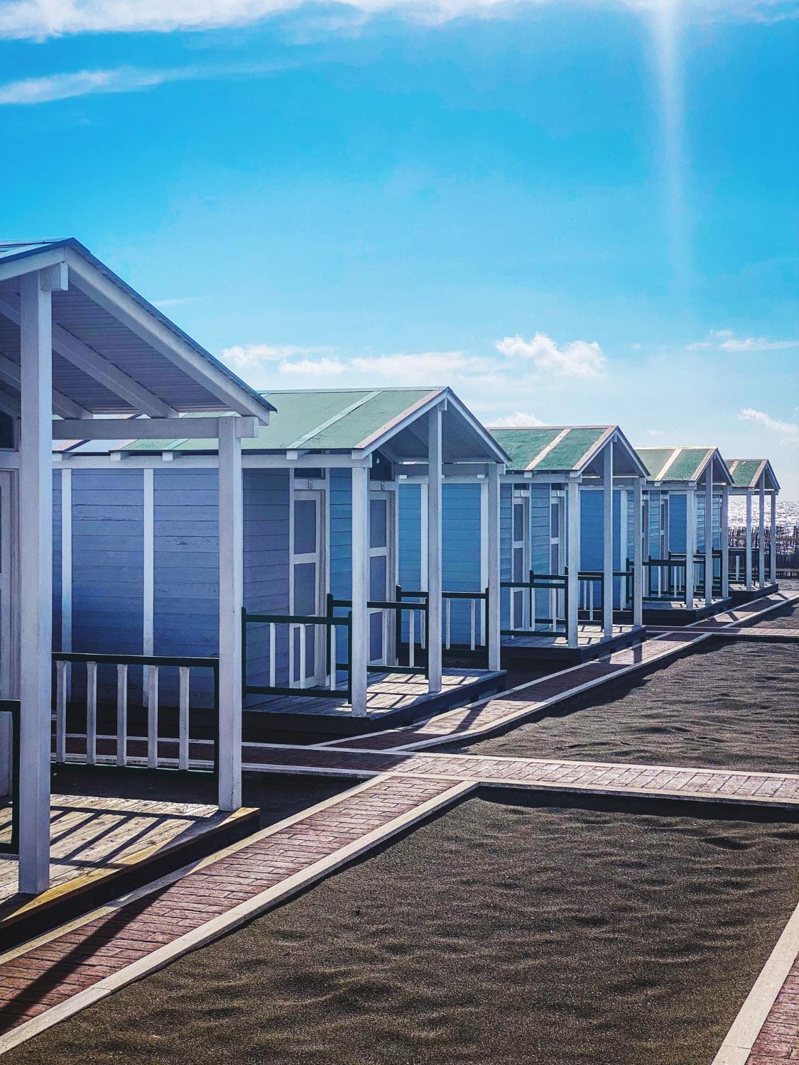 Row of light blue beach huts under a bright blue sky, casting long shadows.