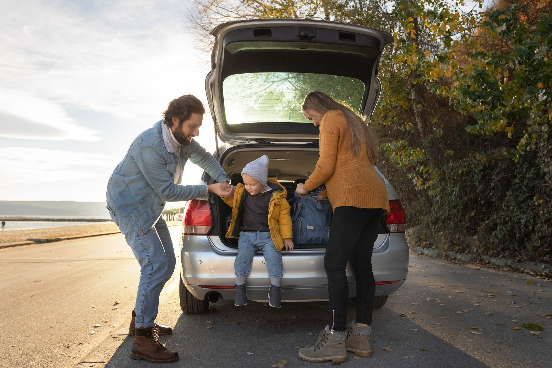 Family loading bags into car trunk outdoors. Sunny day, by the water.