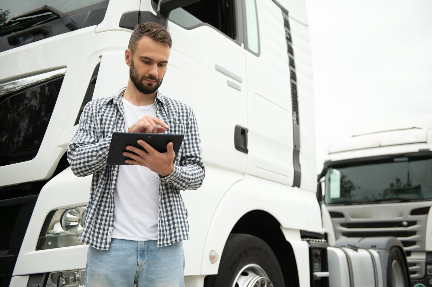 Truck driver using a tablet in front of a white semi-truck.