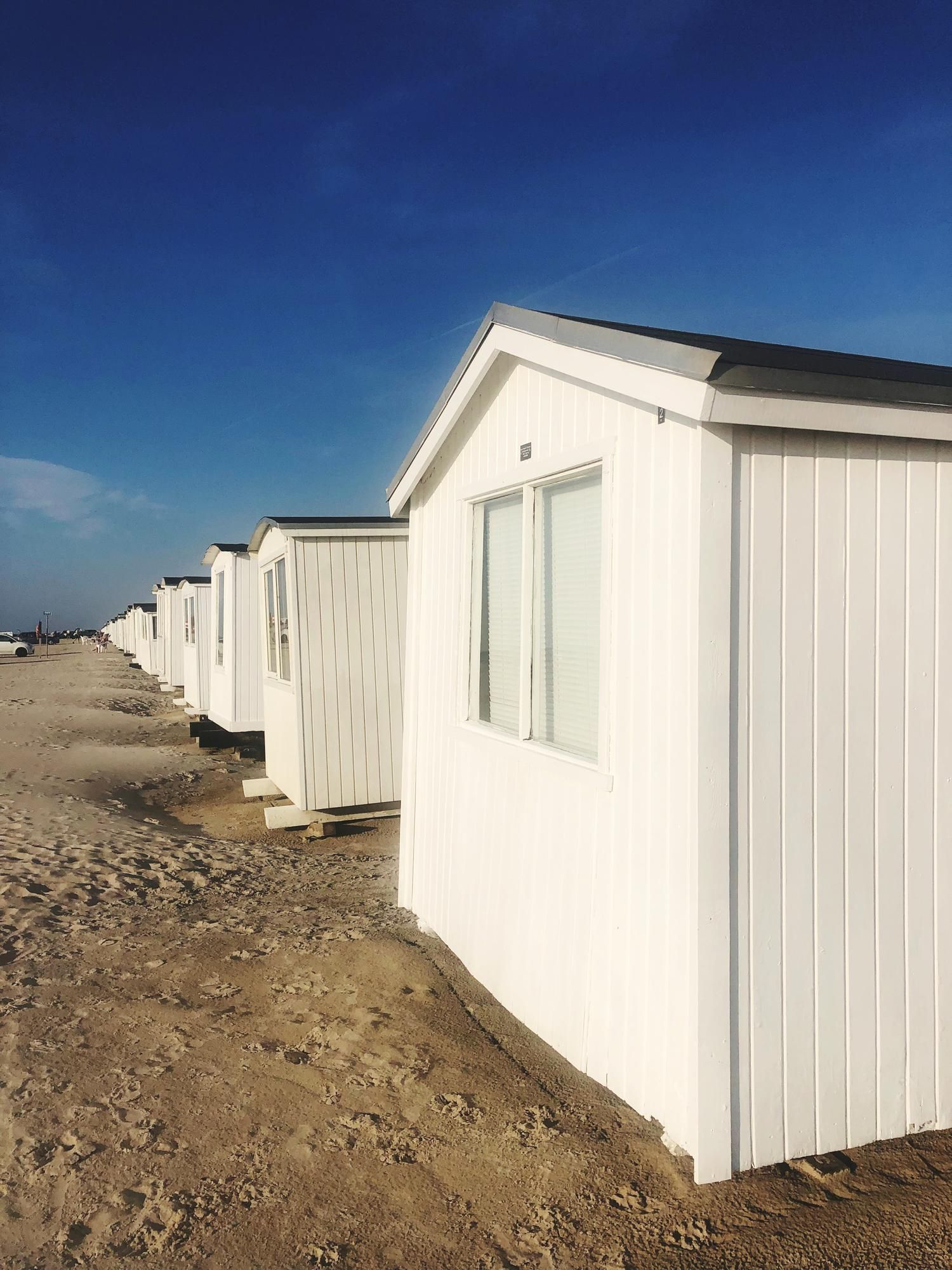 White beach huts lined up, under a bright blue sky.