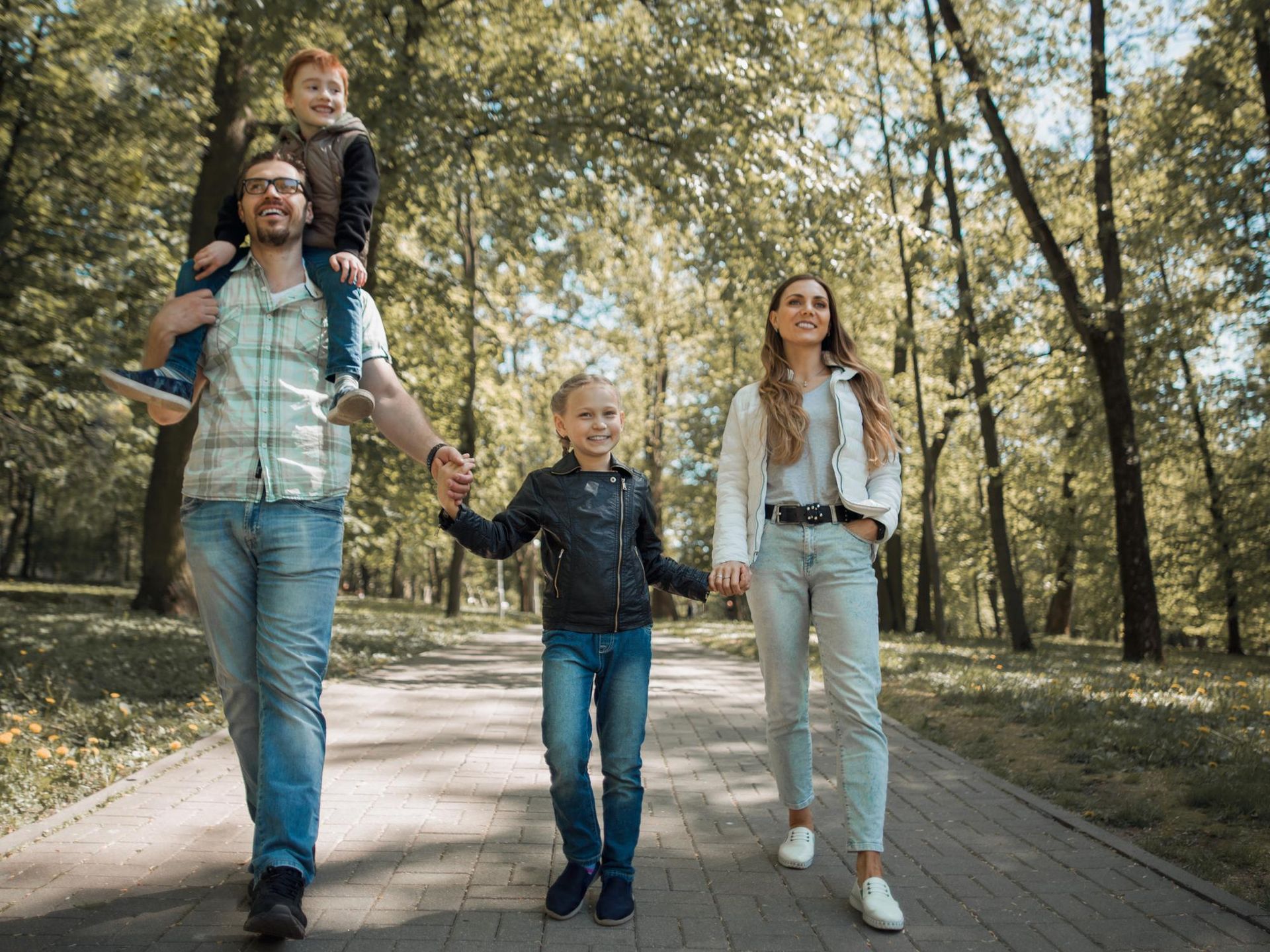 Family walking on a paved path in a park. The father carries a child on his shoulders.