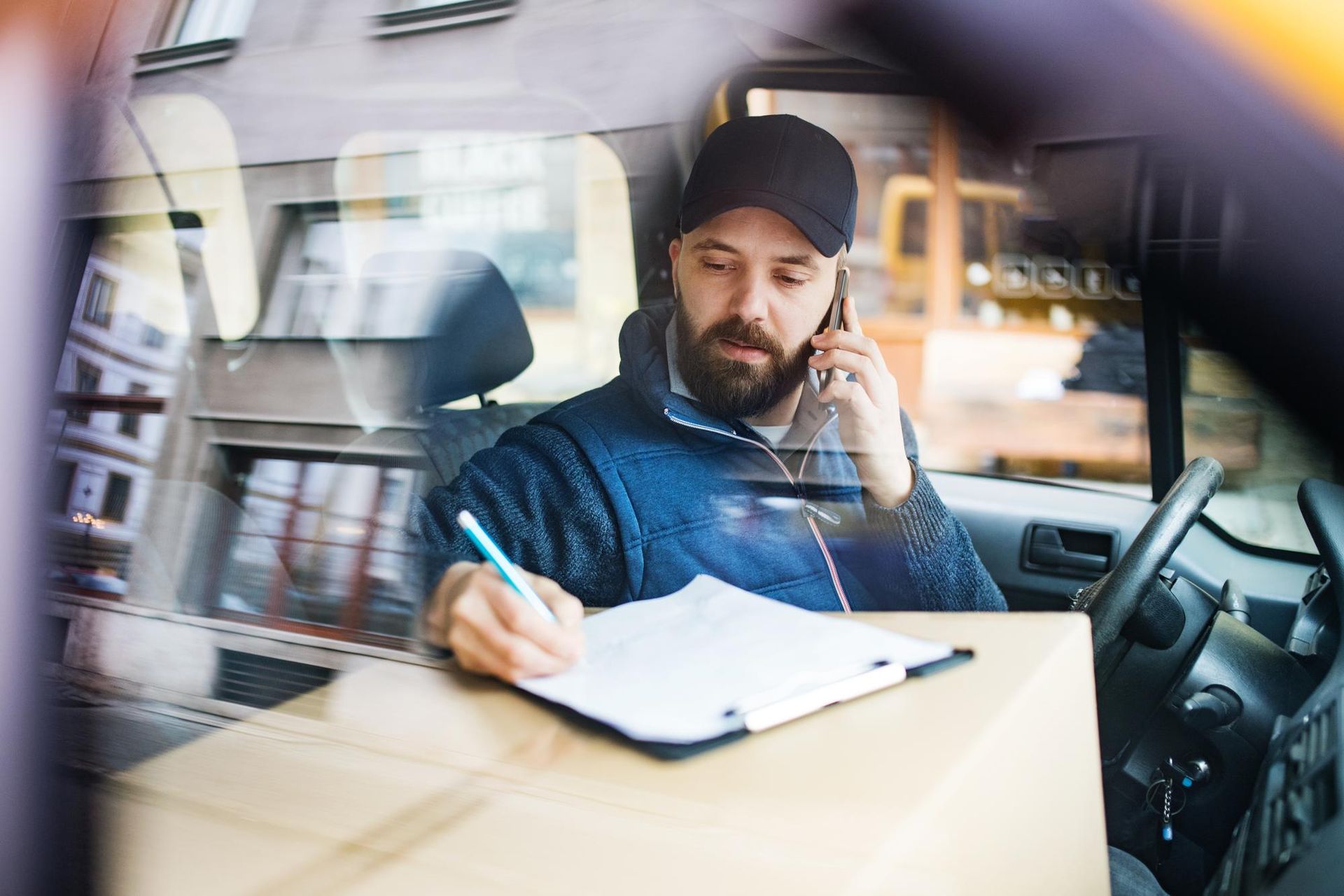 Delivery driver in a van, taking notes on a clipboard while talking on the phone.