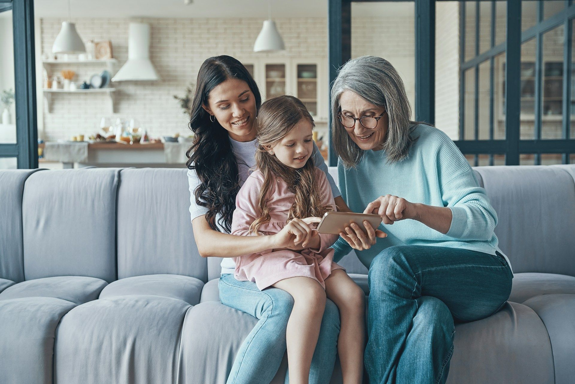 Woman, girl, and senior looking at tablet together on a couch.