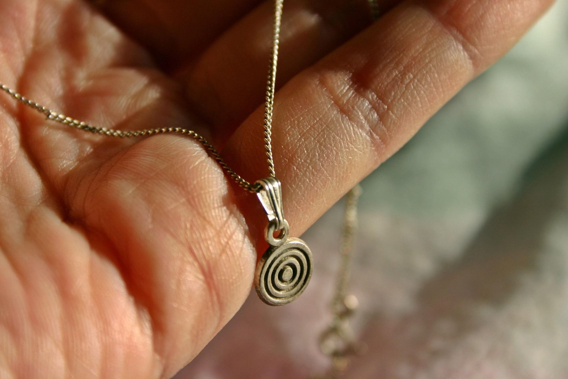 Hand holding a silver necklace with a spiral pendant.