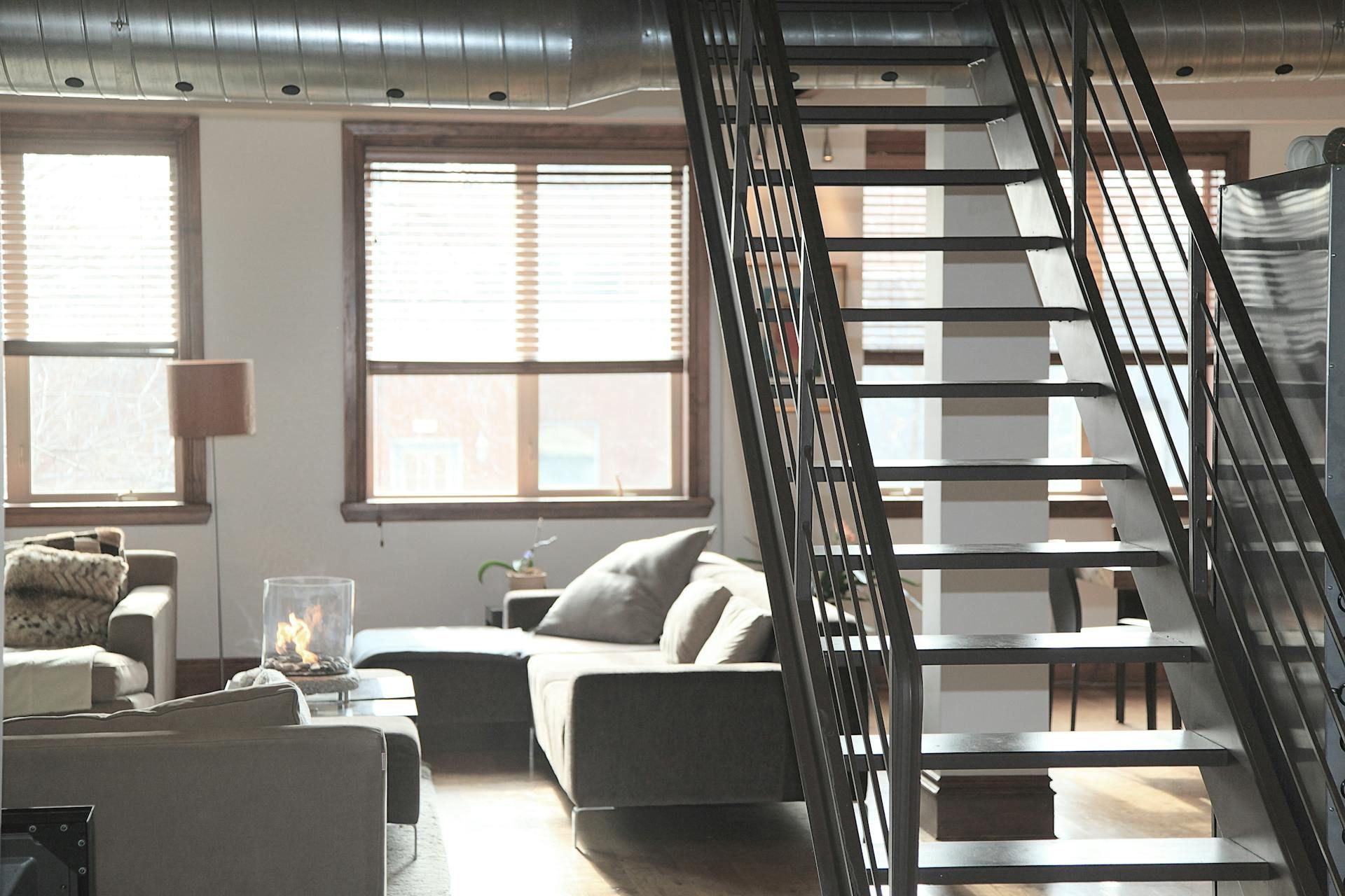 Living room with stairs, windows, sofa, and modern industrial design.
