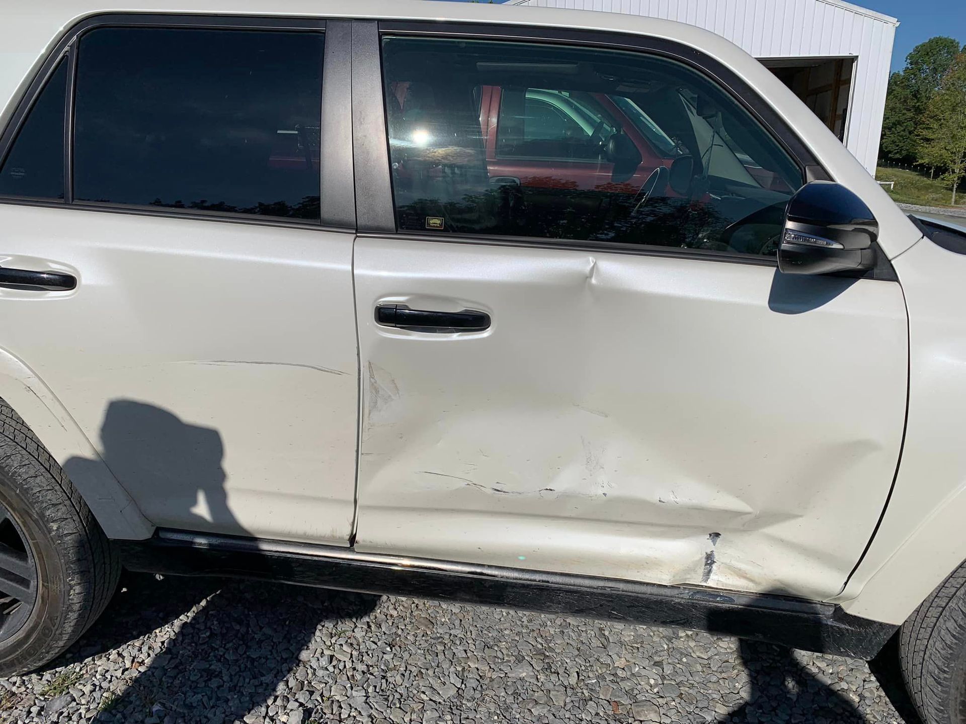 a white suv with a damaged door is parked in a gravel lot .