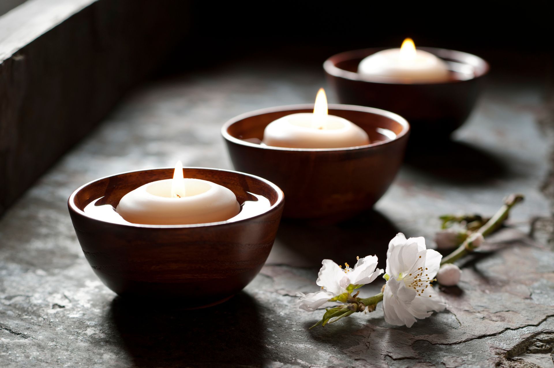 Three bowls filled with candles and flowers on a table.