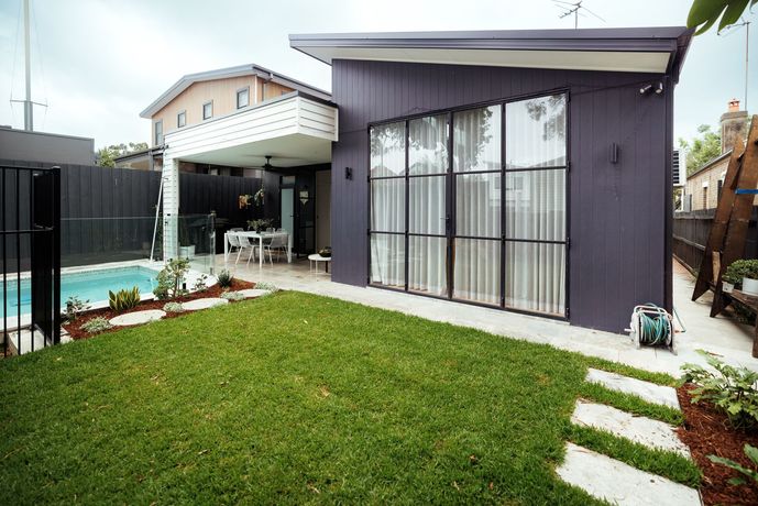 Modern home exterior with a lawn, pool, and dark gray siding with large windows.